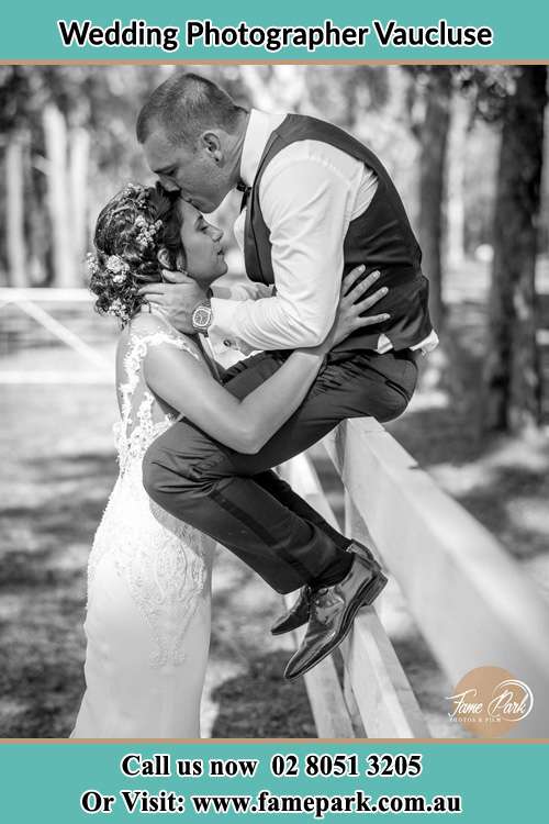 Photo of the Groom sitting at the fence while kissing the Bride on the forehead Vaucluse NSW 2030